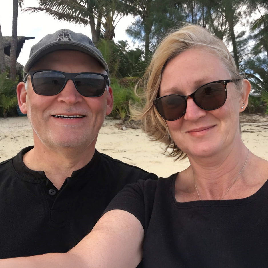 Two people wearing sunglasses on a beach with palm trees in the background